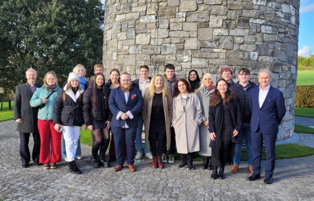 Image of the group (18 people) who took part in the Youth Symposium. They are standing in front of the large central stone tower in the Island Of Ireland Peace Park. 